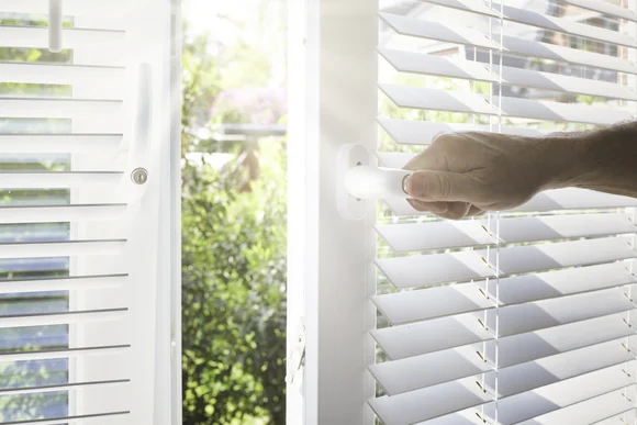 Hand öffnet Fenster mit Jalousien